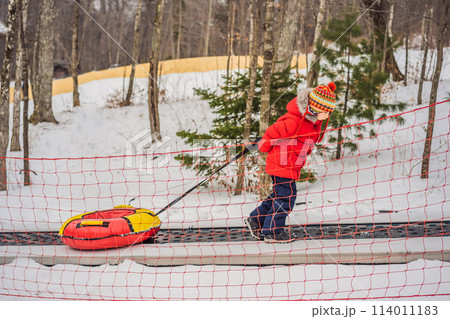 Boy with tubing rises on a travelator to the mountain. Child having fun on snow tube. Boy is riding a tubing. Winter fun for children 114011183