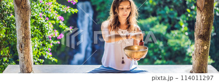 Woman playing on Tibetan singing bowl while sitting on yoga mat against a waterfall. Vintage tonned. Beautiful girl with mala beads meditating BANNER, LONG FORMAT Woman playing on Tibetan singing bowl while sitting on yoga mat against a waterfall. Vintage tonned. Beautiful girl with mala beads meditating BANNER, LONG FORMAT 114011297