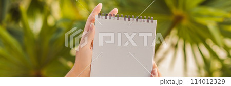 Women's hands in a tropical background holding a signboard, drawing block, paper, mockup BANNER, LONG FORMAT 114012329