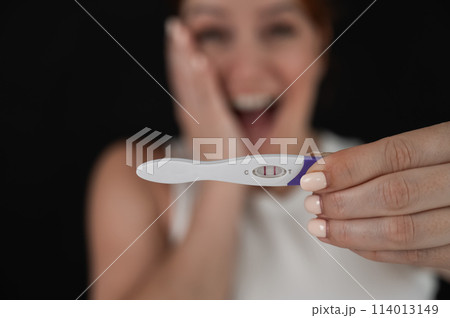 Blurred portrait of happy caucasian woman holding positive express pregnancy test on black background. Blurred portrait of happy caucasian woman holding positive express pregnancy test on black background. 114013149