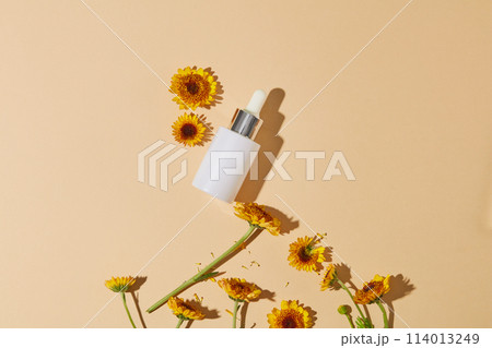 Empty label serum bottle decorated against the background in beige color with fresh Calendula flowers. Calendula extract is known for its antifungal and antibacterial properties 114013249