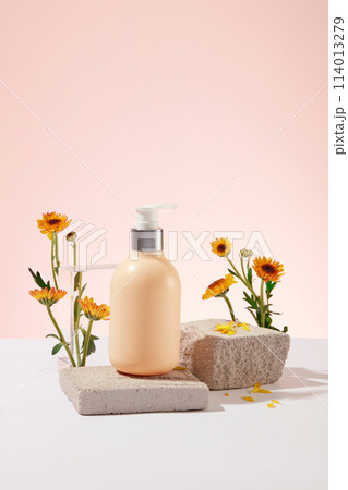 Pump bottle without label standing on a block of stone with branches of Calendula flowers. Front view. Natural cosmetic concept. Empty label for branding mockup Pump bottle without label standing on a block of stone with branches of Calendula flowers. Front view. Natural cosmetic concept. Empty label for branding mockup 114013279