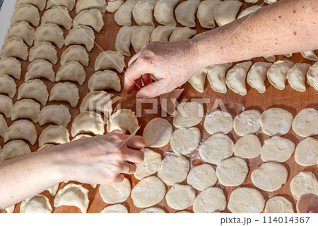 Female hands are making a damp dumpling. On the wooden counter Female hands are making a damp dumpling. On the wooden counter 114014367