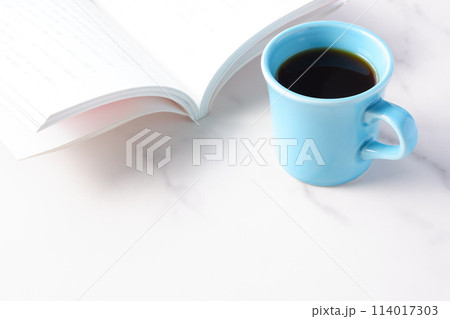 テーブルの上の開いた本とコーヒーカップで、コーヒーを飲みながら読書を楽しむイメージ 114017303