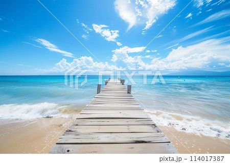 Sundrenched beach and wooden pier under a bright blue sky, perfect for a tranquil day by the sea 114017387