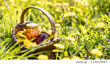 Dandelion flowers in a wicker basket with a jar of honey placed on the ground somewhere in a meadow Dandelion flowers in a wicker basket with a jar of honey placed on the ground somewhere in a meadow 114019947