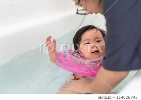 Asian little baby girl swimming and wear rubber ring on neck in bathtub, Mother holding daughter for safety support, Living lifestyle family indoors concept. 114026745