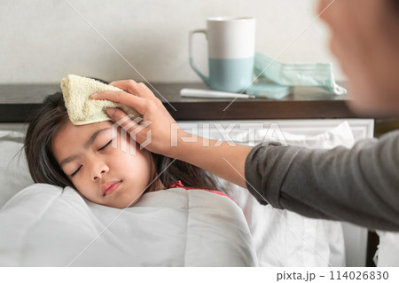 Asian mother take cool towel for reduce high fever on sick girl forehead on bed at morning time, Selective focus, Healthy and infection concept Asian mother take cool towel for reduce high fever on sick girl forehead on bed at morning time, Selective focus, Healthy and infection concept 114026830