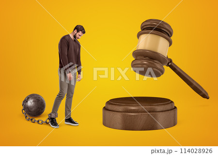 Distressed young man chained to shackle ball and huge browngavel Distressed young man chained to shackle ball and huge browngavel 114028926