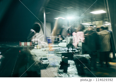 Reflection in the window at passengers and their luggage walking along the boarding corridor of the aircraft from the terminal to the plane. High quality photo 114029392