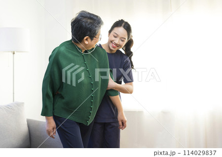 Female Asian nurse help old lady stand up from a couch. Female Asian nurse help old lady stand up from a couch. 114029837