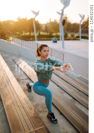 Young woman in sports outfit doing exercises outdoors in the morning. Woman doing stretching exercise. Young woman in sports outfit doing exercises outdoors in the morning. Woman doing stretching exercise. 114032101