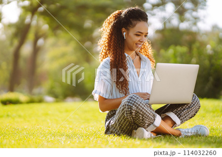 Young woman freelancer sitting on green grass with laptop. Education online. Young woman freelancer sitting on green grass with laptop. Education online. 114032260