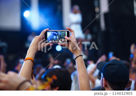 Hand with a phone records live music festival. People taking photographs with smart phone. Hand with a phone records live music festival. People taking photographs with smart phone. 114032905