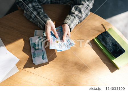 Closeup top view of unrecognizable woman counting stack of euro banknotes at home on sunny day. Close-up of housewife counting cash sitting at table. Concept of investment, money exchange. 114033100