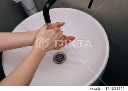 Closeup top view of unrecognizable woman washing dirty hands rubbing using sanitizer soap, rinsing under warm running water above bathroom sink. Concept of hygienic procedures in home bathroom. Closeup top view of unrecognizable woman washing dirty hands rubbing using sanitizer soap, rinsing under warm running water above bathroom sink. Concept of hygienic procedures in home bathroom. 114033153