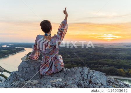 teenage girl in dress, with short-cropped hair, on top cliff, on river bank, at sunset 114033652