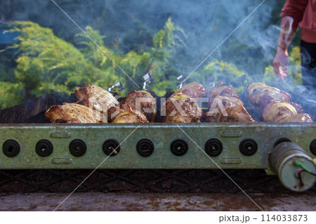 Cooking kebabs on a grill with smoke. Fresh brown BBQ meat cooked on an outdoor grill 114033873