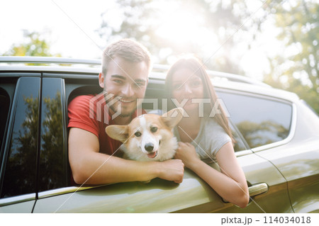 Lovely young couple with dog sits in back seat of car. Concept of active lifestyle, weekend, relax. Lovely young couple with dog sits in back seat of car. Concept of active lifestyle, weekend, relax. 114034018