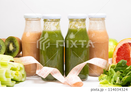 Healthy bottled smoothies among vegetables and fruits and measuring tape. 114034324