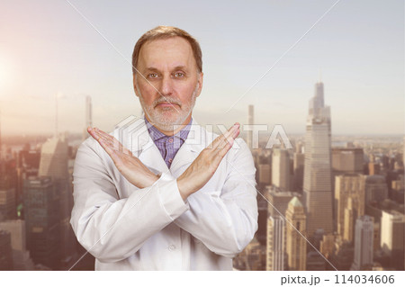 Happy senior medic doctor in white coat shows no reject sign. Urban cityscape background. 114034606