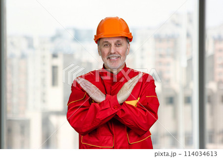 Smiling old caucasian worker shows the sign of prohibition. Bright urbanscape background. Smiling old caucasian worker shows the sign of prohibition. Bright urbanscape background. 114034613
