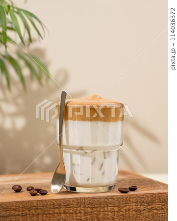 Dalgona coffee. Whipped instant coffee in a glass on a wooden stand with coffee beans 114036372