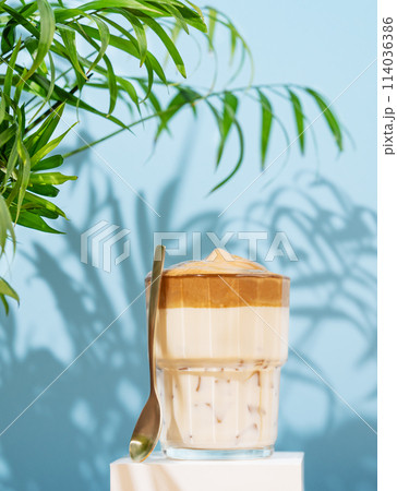 Dalgona coffee. Whipped instant coffee in a glass on a white stand with coffee beans Dalgona coffee. Whipped instant coffee in a glass on a white stand with coffee beans 114036386