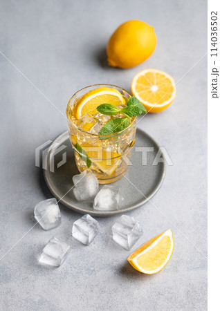 Iced tea with lemon, mint and ice in a glass on a light background with citrus fruits. 114036502