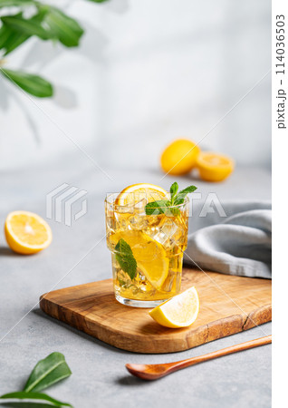 Iced tea with lemon, mint and ice in a glass on a wooden board on a light background with shadow 114036503