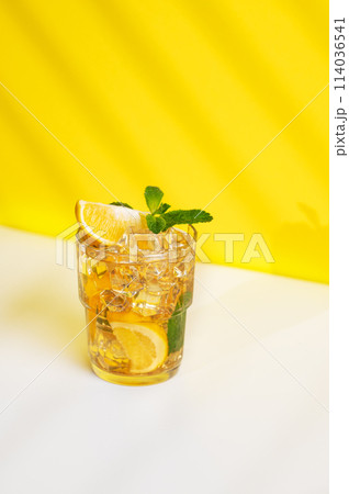 A glass of iced tea with lemon and mint on a yellow and white background with a shadow. A glass of iced tea with lemon and mint on a yellow and white background with a shadow. 114036541