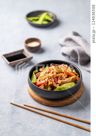 Stir-fry with soba noodles, meat and vegetables on a light background with chopsticks, soy sauce 114036588