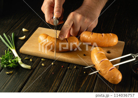 The cook prepares Vienna sausages on the kitchen board. Grill cooking concept with sausages and aromatic spices. Space for recipe or menu The cook prepares Vienna sausages on the kitchen board. Grill cooking concept with sausages and aromatic spices. Space for recipe or menu 114036757