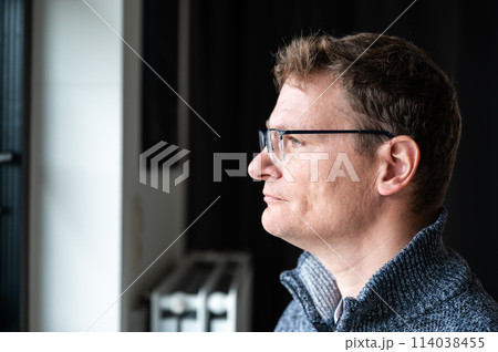Indoor portrait of a 45 yo white man looking through his window at home, Brussels, Belgium Indoor portrait of a 45 yo white man looking through his window at home, Brussels, Belgium 114038455