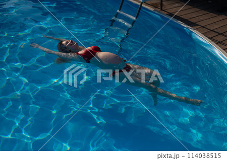 Top view of pregnant woman floating in pool in red bikini. Top view of pregnant woman floating in pool in red bikini. 114038515