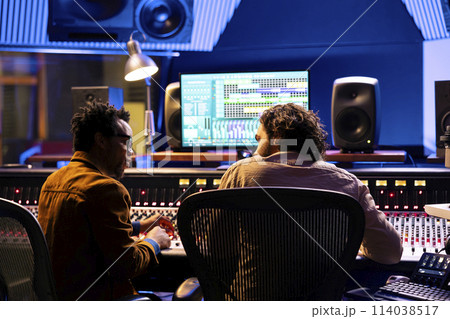 Team of sound technician and singer working on new music, mixing tunes on digital software in control room. Musician and producer collaborating on a new album, mixing and mastering tracks. 114038517