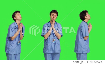 Medical assistant being hopeful praying for good luck against greenscreen, holds hands in a prayer sign and having belief in spirituality. Young christian nurse with faith in meditation. Camera B. 114038574