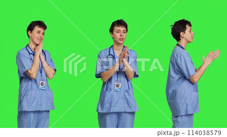 Smiling medical assistant applauding someone in studio, celebrating success and cheering against greenscreen backdrop. Young nurse clapping hands and feeling happy about achievement. Camera B. 114038579