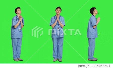 Medical assistant being hopeful praying for good luck against greenscreen, holds hands in a prayer sign and having belief in spirituality. Young christian nurse with faith in meditation. Camera A. 114038601