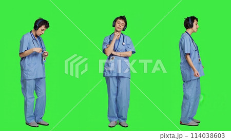 Cheerful health specialist listening to cool music on audio headset, dancing against greenscreen backdrop and having fun. Nurse enjoying songs an doing funny dance moves, leisure. Camera A. 114038603