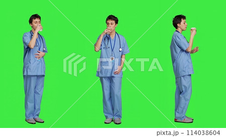 Healthcare specialist enjoying hot coffee cup against greenscreen backdrop, drinking caffeine refreshment in blue scrubs. Medical assistant serving beverage at work, friendly staff. Camera A. Healthcare specialist enjoying hot coffee cup against greenscreen backdrop, drinking caffeine refreshment in blue scrubs. Medical assistant serving beverage at work, friendly staff. Camera A. 114038604