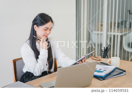 Smiling millennial Asian female office worker working with financial reports for tax audit reports or financial statement in a meeting room. Smiling millennial Asian female office worker working with financial reports for tax audit reports or financial statement in a meeting room. 114039581