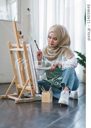 Muslim young female artist painting on canvas at home. Hobby and leisure concept. 114039648