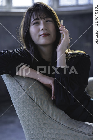 シックな部屋のソファでスマホで電話する若い女性 シックな部屋のソファでスマホで電話する若い女性 114040101