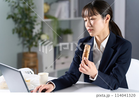 夜食を食べながら仕事をするビジネスウーマン 夜食を食べながら仕事をするビジネスウーマン 114041320