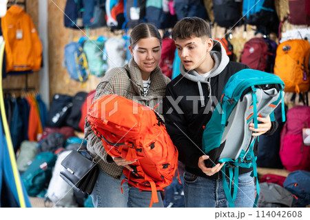 Young married couple in winter clothes chooses a durable backpack for a winter hike in tourist equipment store Young married couple in winter clothes chooses a durable backpack for a winter hike in tourist equipment store 114042608