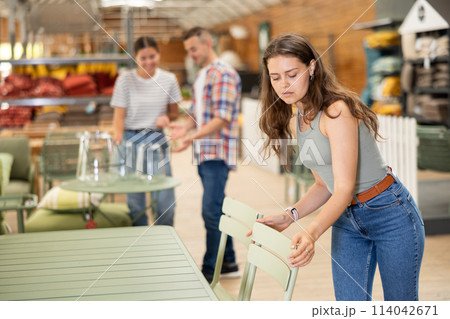 Pensive girl choosing patio chairs at garden furniture store 114042671