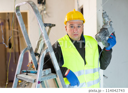 Portrait of builder handyman working with electric drill in repairable room 114042743