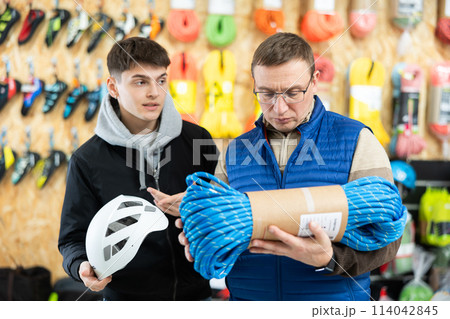 Father and his adult son carefully select a safety helmet and a climbing rope for a winter hike in sports equipment store Father and his adult son carefully select a safety helmet and a climbing rope for a winter hike in sports equipment store 114042845
