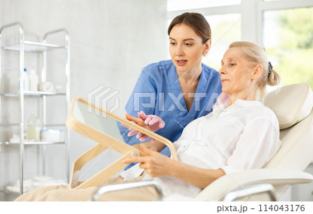 Female cosmetologist explaining facial procedure to elderly woman Female cosmetologist explaining facial procedure to elderly woman 114043176